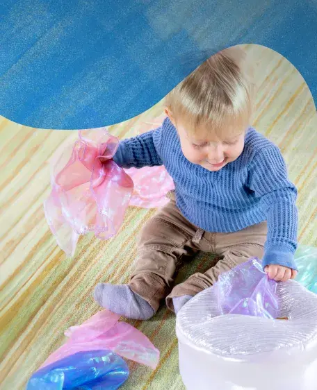 Baby on the floor pulling pastel colored tissues out of the Sensory Surprise Tissue Box