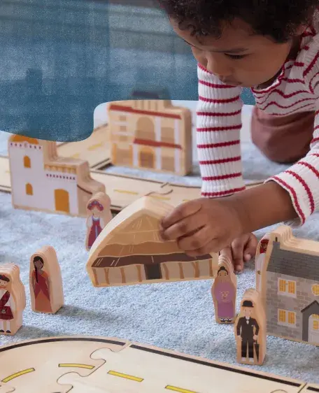 Young boy placing a block shaped like a hut on a carpeted floor with other house-shaped blocks arranged around him