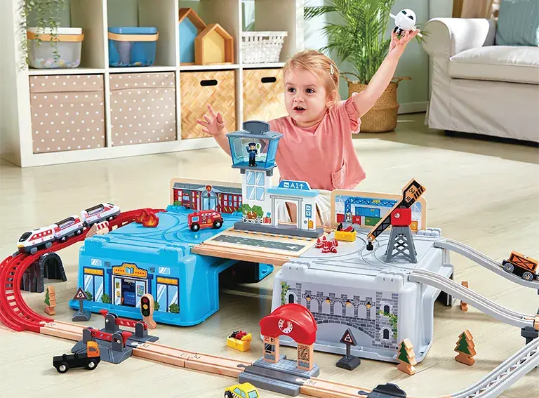 Small child playing with a large train and automobile playset with tracks and buildings