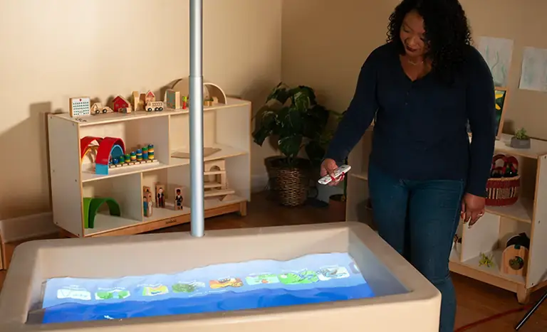 Woman demonstrating the operation of the Illumination Station augmented reality sand table