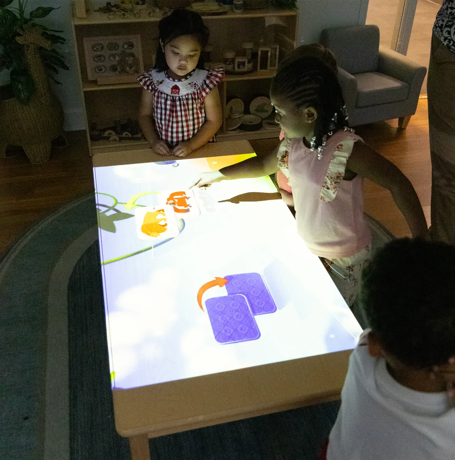 Three children standing around a table using their hands to play a virtual game projected onto a table